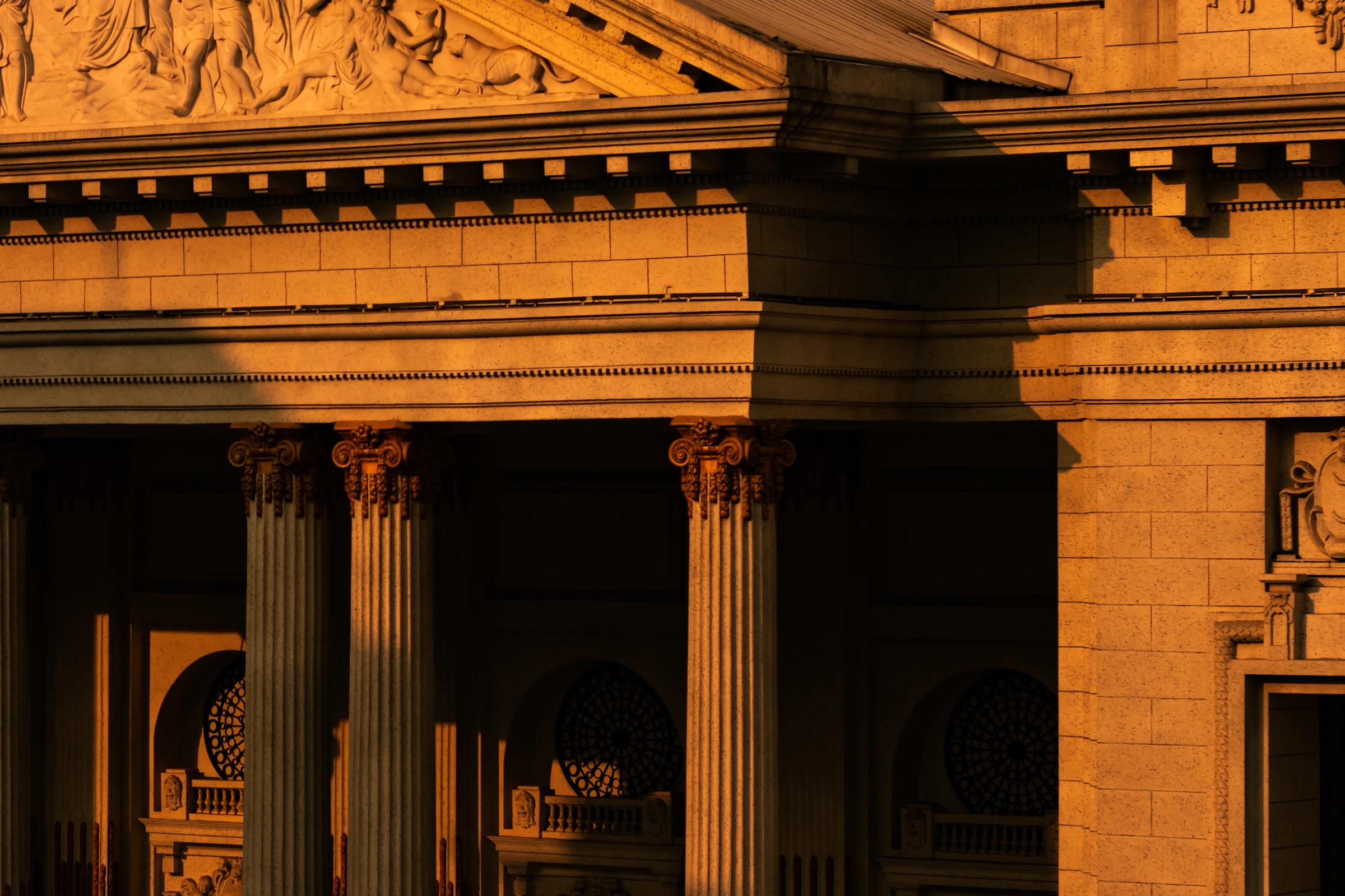 The columns and carved pediment of a classical building in golden evening light.