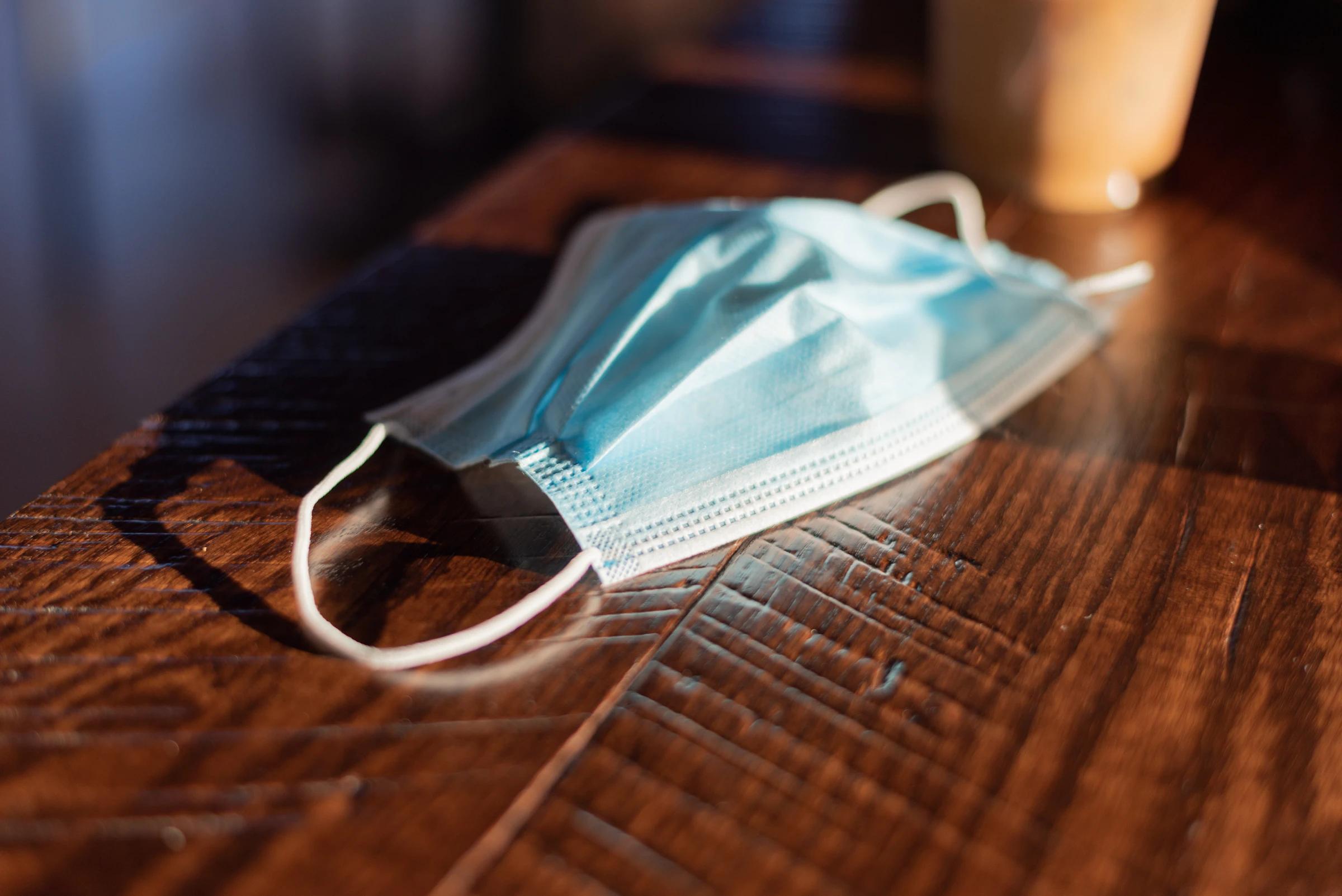 A surgical face mask lying on a sunlit wooden table.